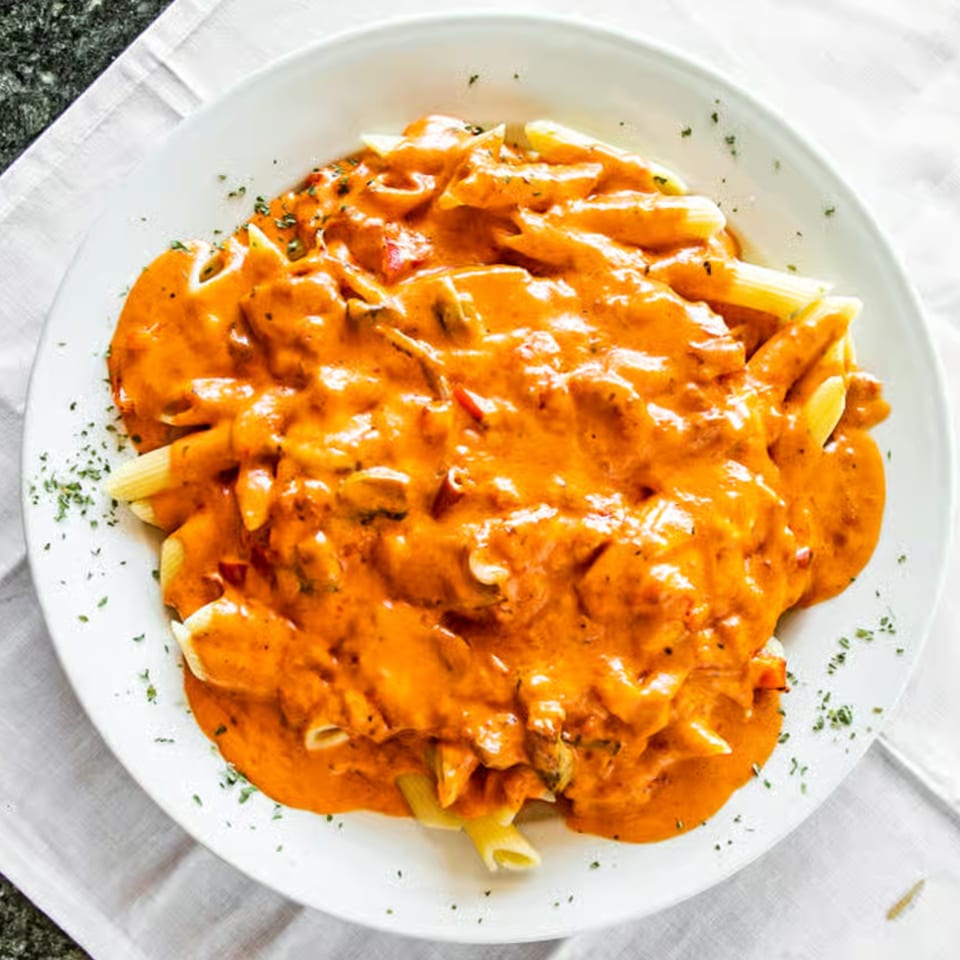 A white plate filled with penne pasta in a creamy orange sauce, garnished with herbs.