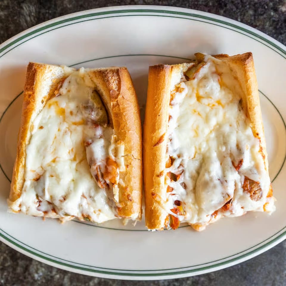 Two halves of a cheesy steak and onion sub sandwich on a white plate with a green rim.