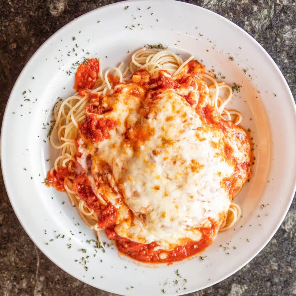 Spaghetti with red sauce and melted mozzarella cheese, garnished with herbs on a white plate.