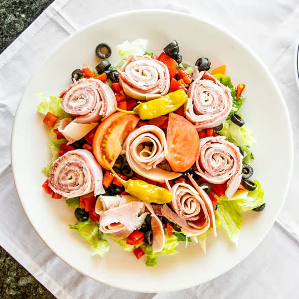 A Sali's Pizza & Pasta antipasto salad with rolled meats, lettuce, tomatoes, olives, and peppers.