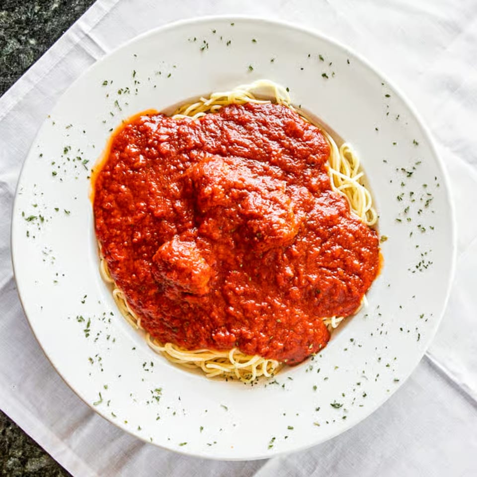 A white plate of spaghetti with meatballs and red sauce, garnished with herbs.
